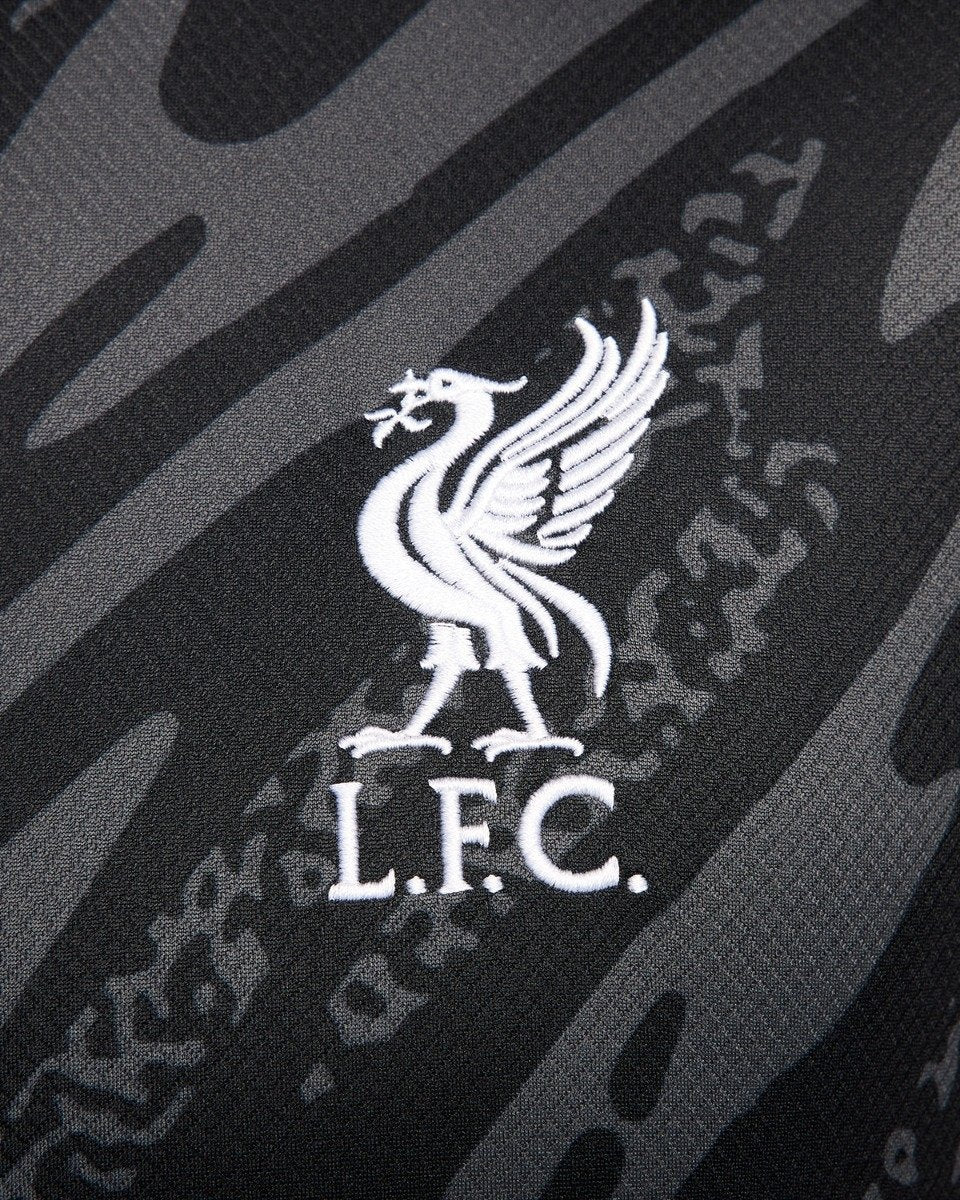 ttlJuVWx5mwfNHB_fe05e79b-b68e-4d3a-a3fd-4e01e14a92a4 | UAE SPORT STORE White embroidered Liver Bird crest with the letters L.F.C. on dark camouflage fabric, representing Liverpool FC against a textured background