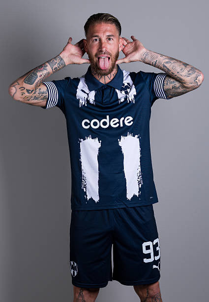 tumblr_2795e1a7bdb014766e3938ff84c193be_97918d59_500 | UAE SPORT STORE Tall man with tattoos wearing a navy soccer jersey and shorts, sponsor 'codere' on chest, number 93, sticking out tongue and pulling ears in a playful pose.