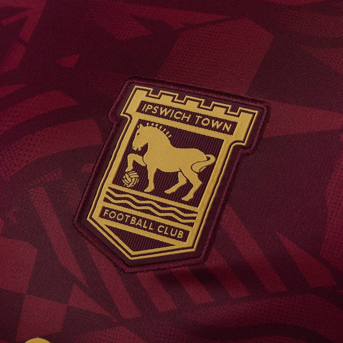 Close-up of the Ipswich Town Football Club crest on a maroon jersey. (patch with gold emblem)
