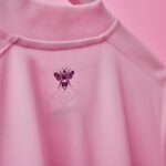 Close-up of a pink fabric with a small black bee emblem on the chest area