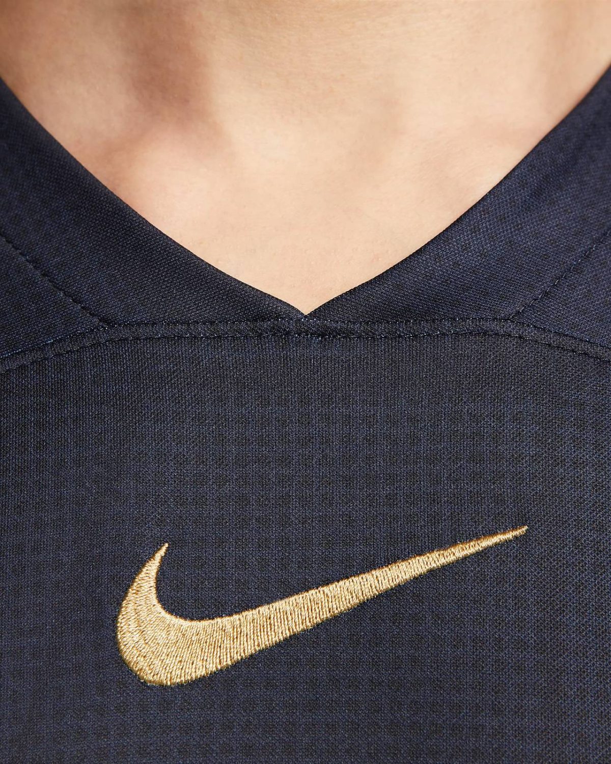 Close-up of dark blue fabric with a gold Nike swoosh embroidered on it.
