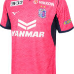 Pink soccer jersey with navy trim and geometric pattern, team crest on chest, YANMAR sponsor across front, Mizuno logo nearby, and NIKKON sponsor above.