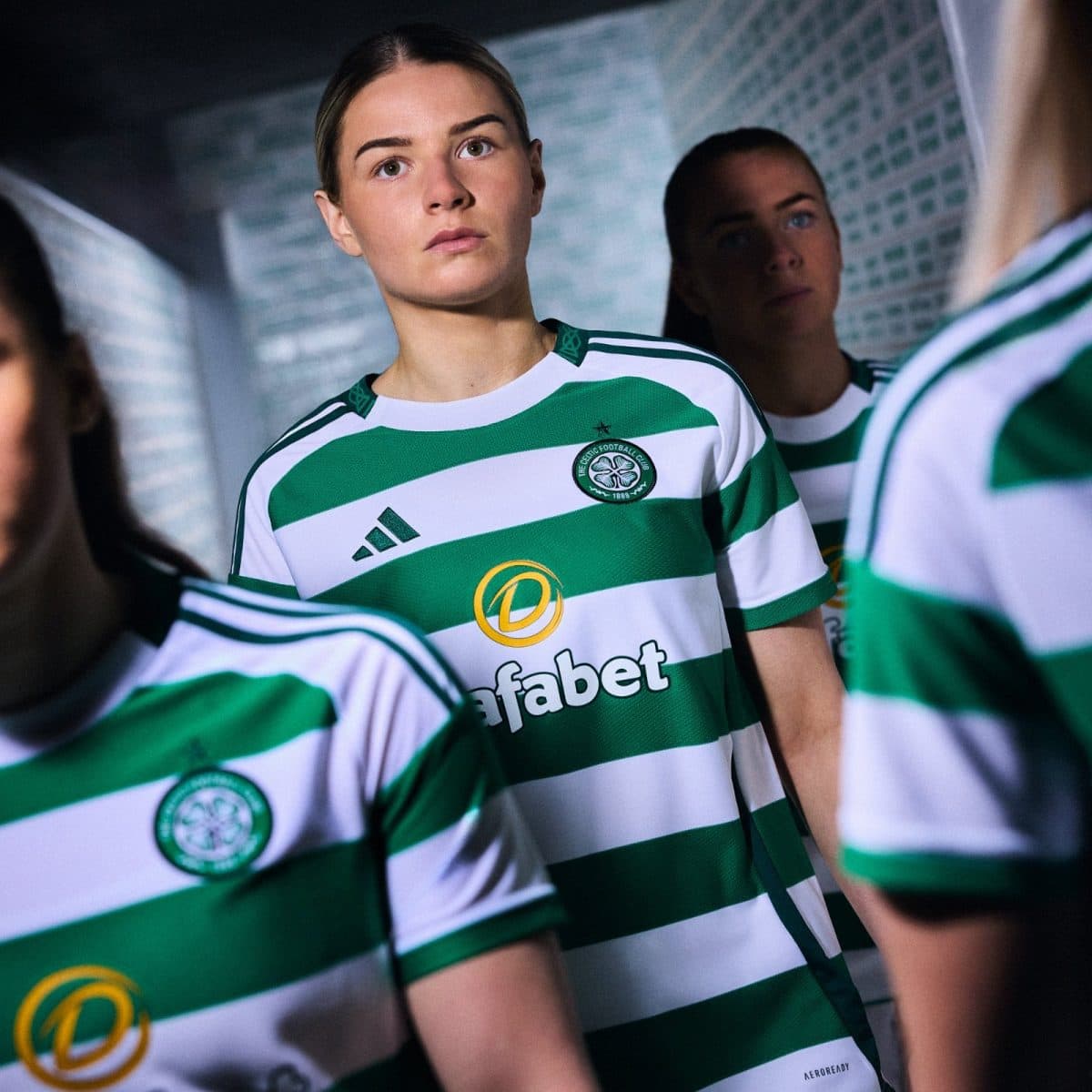 Group of female soccer players in green and white striped jerseys standing in a tunnel, looking ahead with focused expressions.