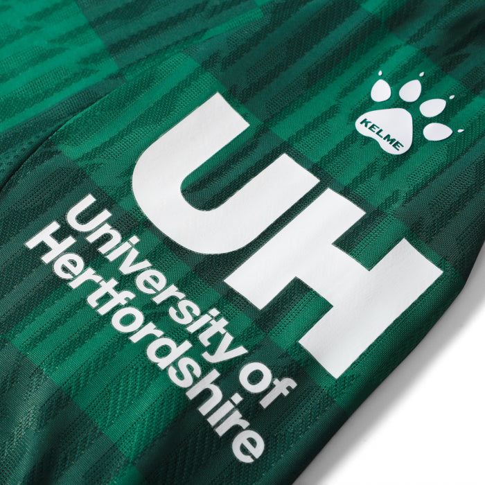 ujjkjkj | UAE SPORT STORE Close-up of a green jersey with large white 'UH' lettering and 'University Of Hertfordshire' text, plus a Kelme paw logo.