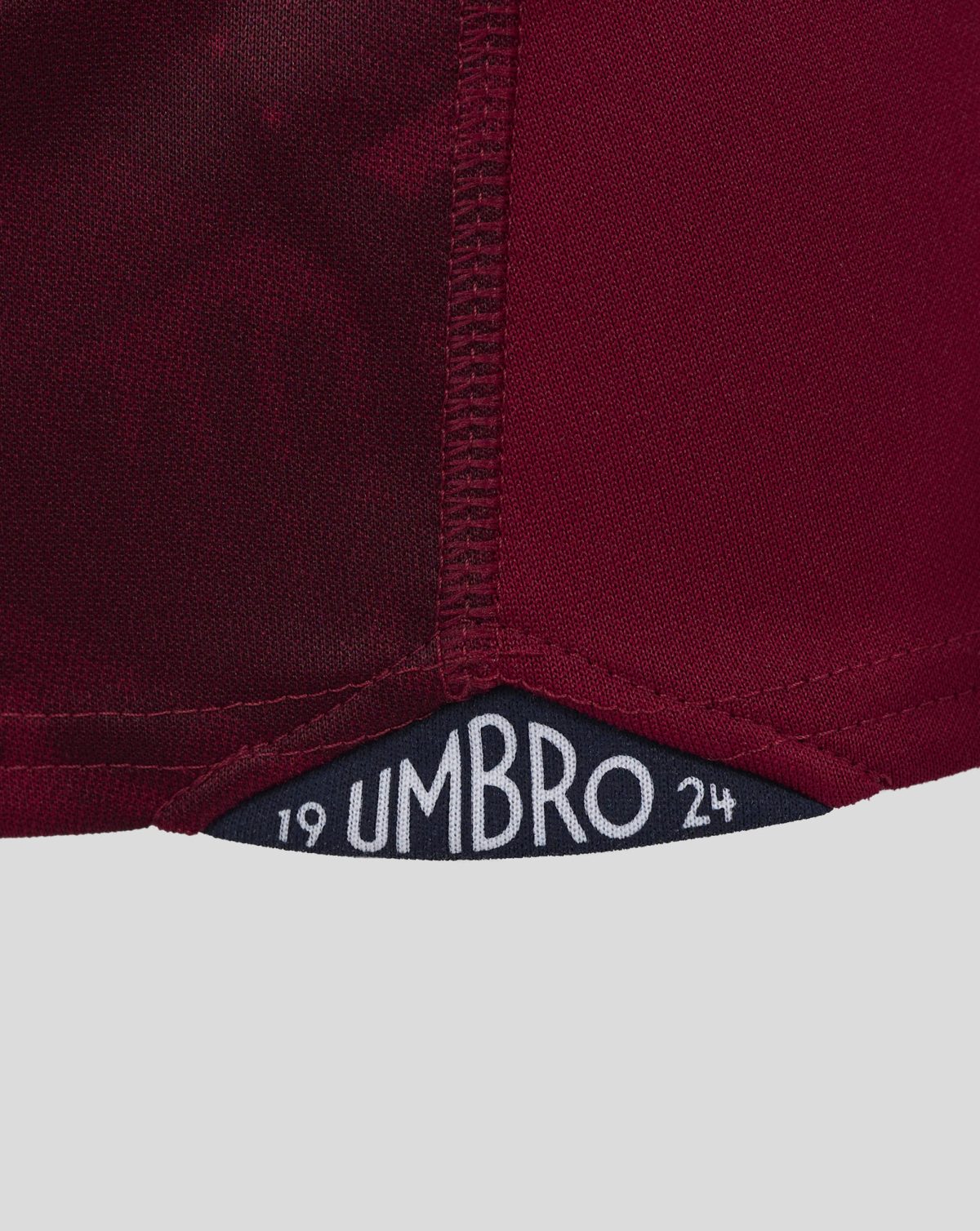 Close-up of burgundy knit fabric with visible stitching and a partial UMBRO label.