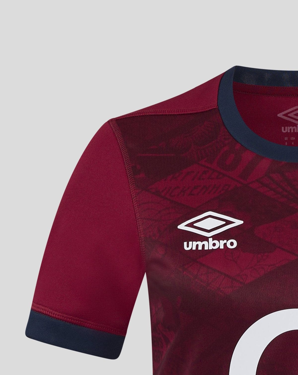 Close-up of a maroon Umbro jersey showing the shoulder seam, navy collar, and partial white logo.