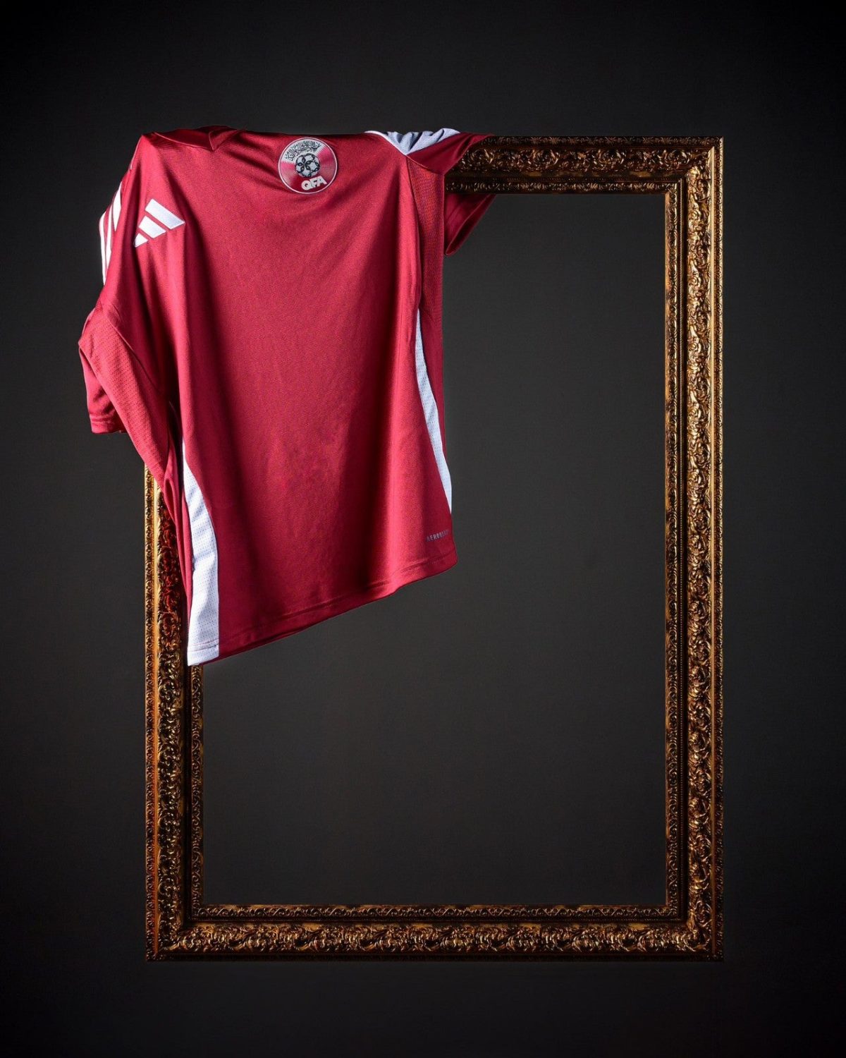 Red athletic jersey with white stripes draped over a gilded ornate frame against a dark background, as if displayed or hung for display.