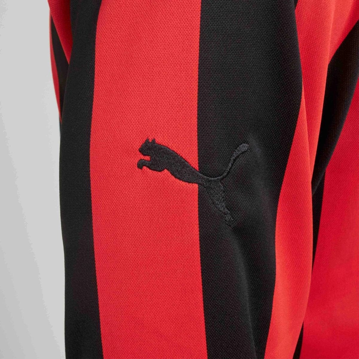 Close-up of a red and black striped sports jersey with a small black Puma logo patch on the fabric.