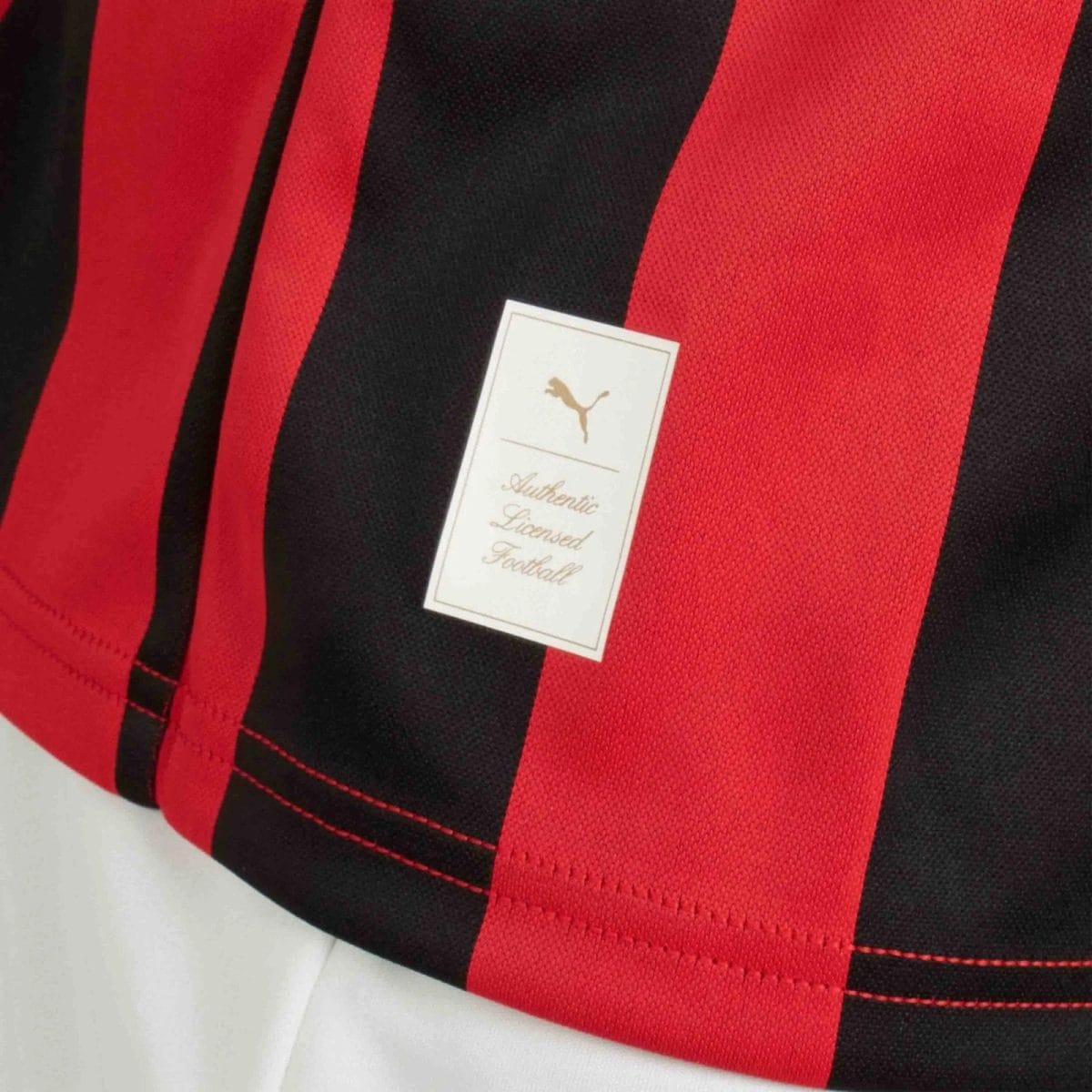 Close‑up of red and black striped sports jersey fabric with a white tag that reads 'Authentic Licensed Football' and shows a Puma logo.