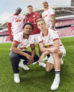Five RB Salzburg players pose on a green pitch inside a large stadium, wearing white and red kits.