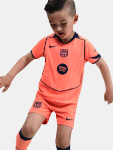 Young boy wearing an orange FC Barcelona soccer kit with Nike swoosh and Spotify sponsor logos, posing dynamically.