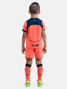 Back view of a child in a bright orange soccer kit with navy accents, UNHCR logo on the shorts, and neon cleats.