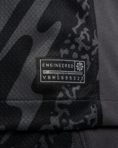 vwq5prN6GkDVRTb_09c878ee-7bc3-423b-8f38-9adf5779c65d | UAE SPORT STORE Close-up of a black camouflage fabric with a rectangular label reading 'ENGINEERED' and a string of characters (VBMS605322).
