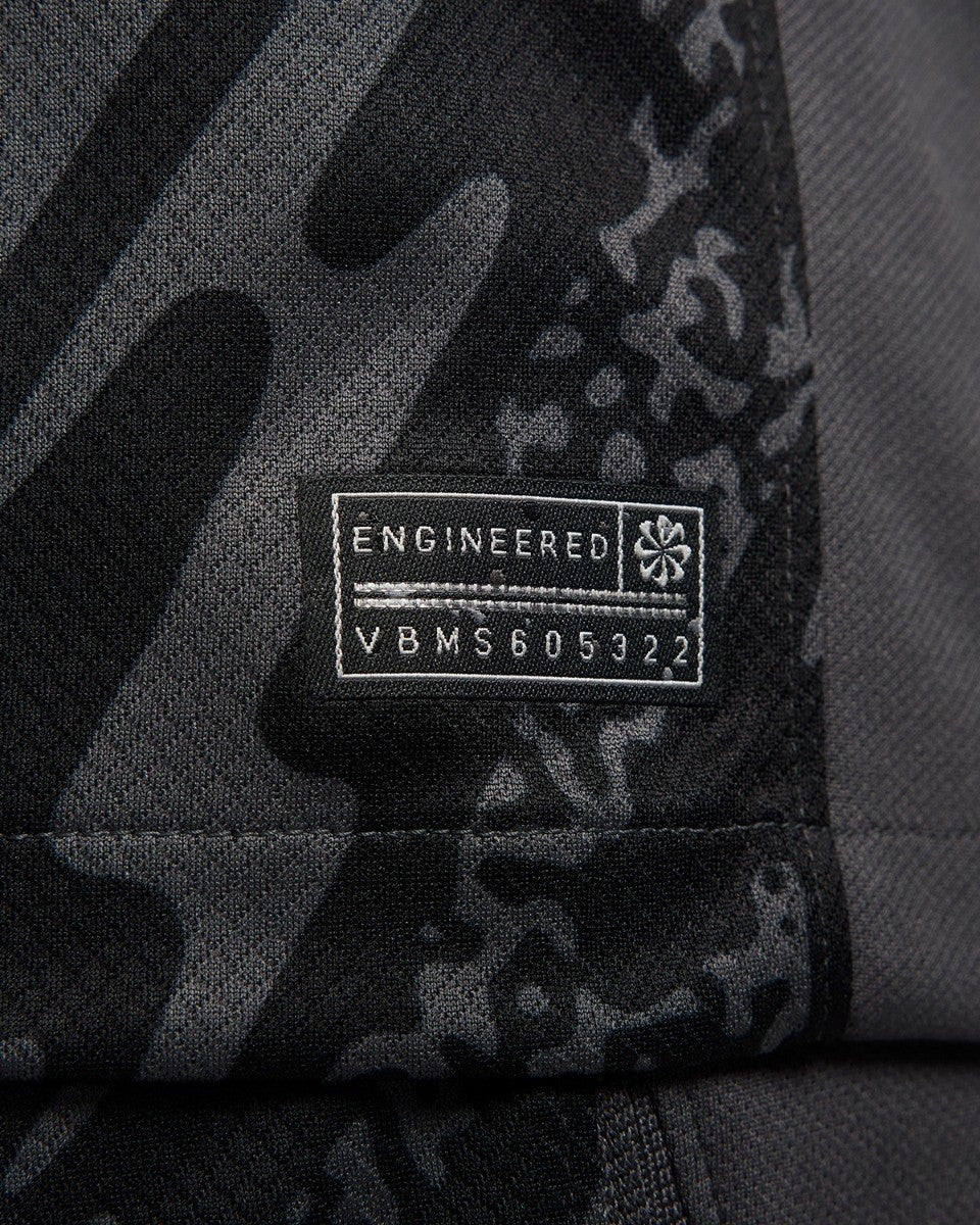 vwq5prN6GkDVRTb_09c878ee-7bc3-423b-8f38-9adf5779c65d | UAE SPORT STORE Close-up of a black camouflage fabric with a rectangular label reading 'ENGINEERED' and a string of characters (VBMS605322).