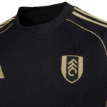 vx | UAE SPORT STORE Black athletic jersey with gold shoulder stripes and a gold crest patch on the chest of the left side.