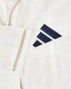 Close-up of a cream backpack fabric with a navy Adidas three-stripe logo, zipper edge and strap detail