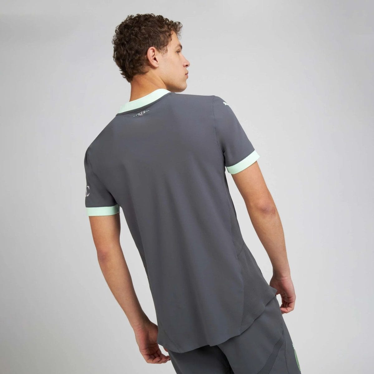 Back view of a person wearing gray scrubs with mint-green cuffs against a light gray background.