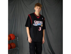 width_538_height_415_quality_90_fit_pad_format_webp_2 | UAE SPORT STORE Young man wearing a black Philadelphia 76ers jersey with number 3, standing beside a metal rack of basketballs against a gray backdrop.