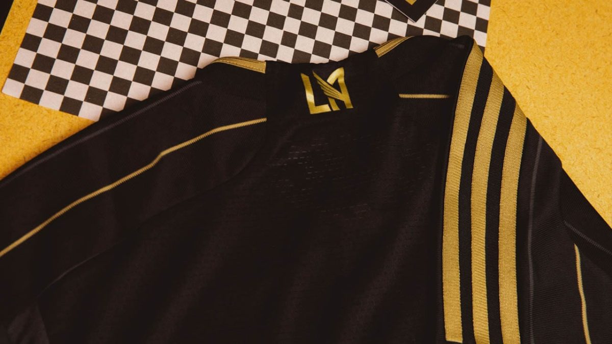 Black varsity jacket with gold stripes laid on a checkered floor, displaying its sleeve and collar details.
