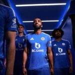 Three footballers in blue BC.GAME jerseys stand in a blue-lit tunnel before a match, focused and ready.