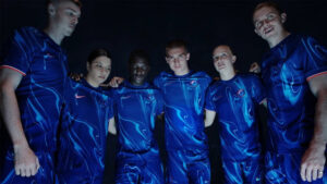 Six team members in blue jerseys standing together with arms around each other in a dim setting.