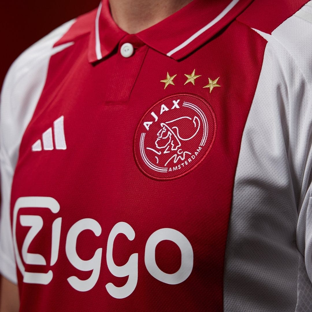 xpCIjTOrvIjll9t | UAE SPORT STORE Ajax football jersey close-up: red shirt with crest, three gold stars, Adidas logo and Ziggo sponsor.
