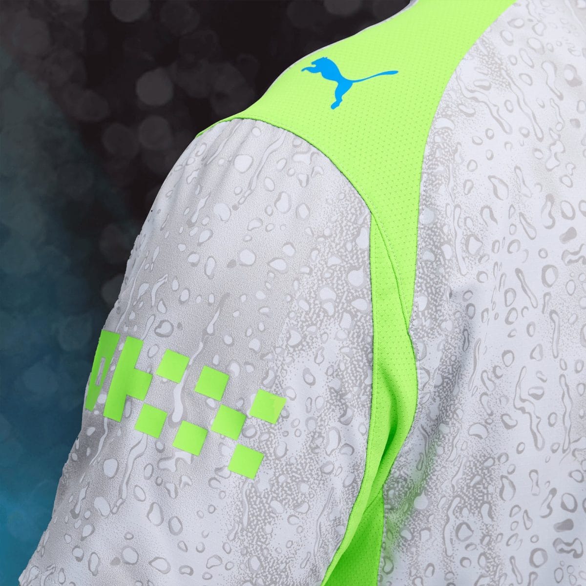 Close-up of a white athletic jacket with neon-green piping and a blue Puma logo, featuring a speckled pattern.
