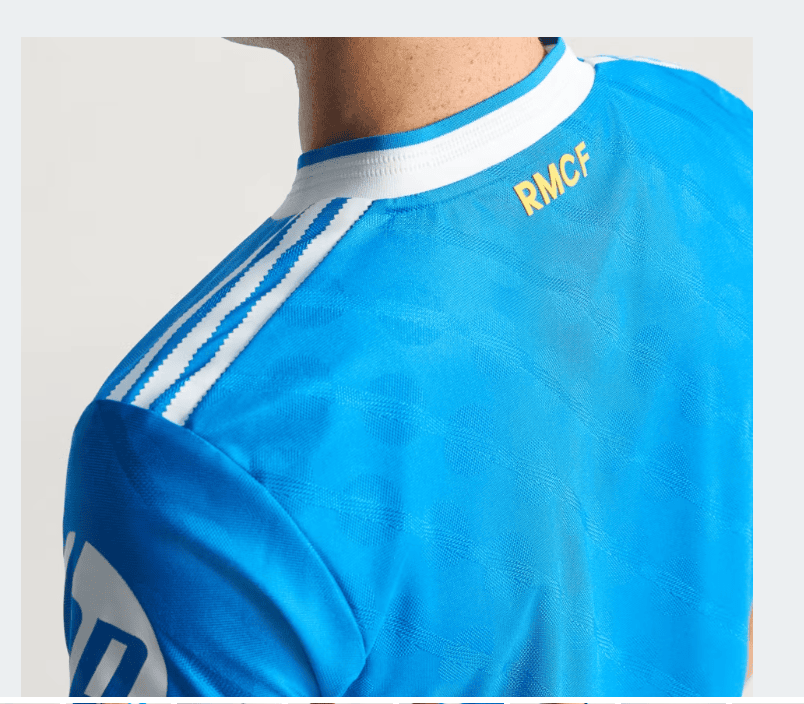 xxxa | UAE SPORT STORE Back view of a blue soccer jersey with white collar and three white stripes on the shoulder, RMCF in gold on the neck area