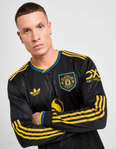 Portrait of a man with short dark hair wearing a black Manchester United jersey with yellow stripes, arms crossed.