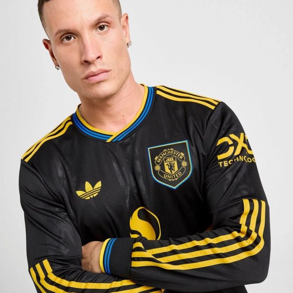 Portrait of a man with short dark hair wearing a black Manchester United jersey with yellow stripes, arms crossed.