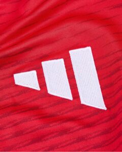 Close-up of red fabric with a white stitched three-stripe Adidas logo on the sportswear tag.