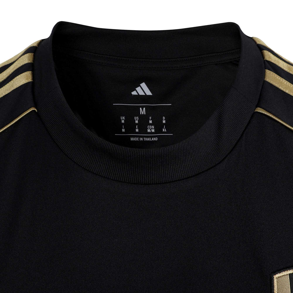 yi | UAE SPORT STORE Close-up of a black shirt collar with gold stripes along the shoulders and an Adidas logo visible on the interior label (size M).