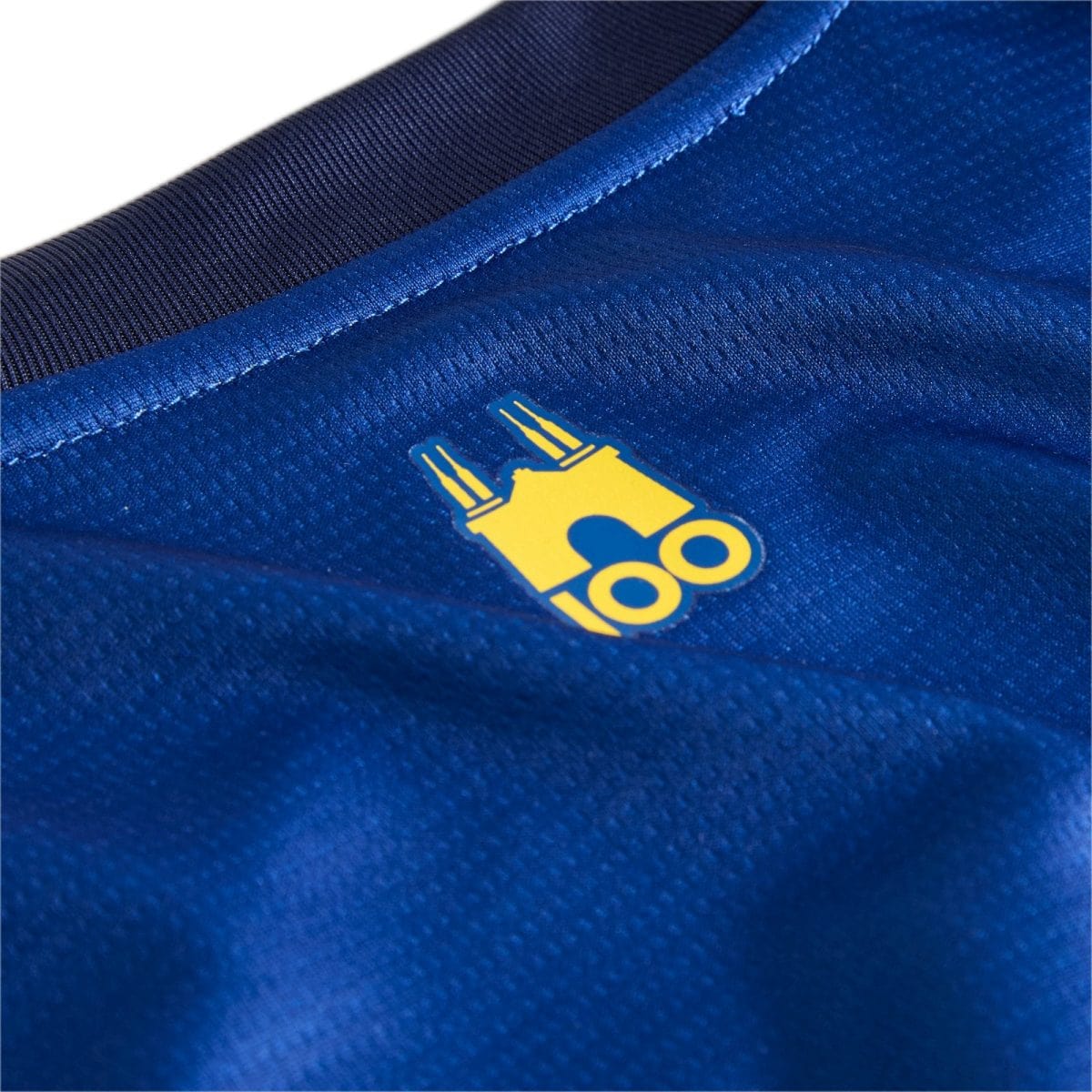 Close-up of blue athletic fabric with a small yellow emblem partially visible near a seam.