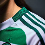 Close-up of a white and green football jersey shoulder with green stripes running along the sleeve and a green collar detail; a partial team badge is visible.