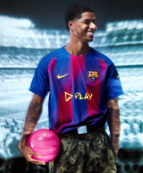 yt | UAE SPORT STORE Smiling male soccer player in FC Barcelona jersey standing in a stadium, holding a pink soccer ball.