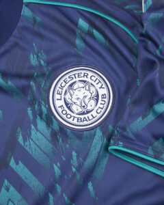 Close-up of a Leicester City Football Club badge on a blue patterned jersey with teal piping.