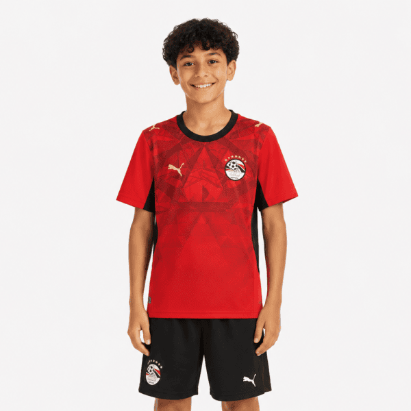 Young boy wearing Egypt home World Cup kids kit 2026 with red jersey and black shorts.
