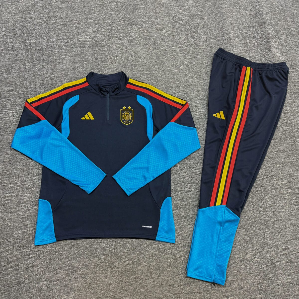 Spain navy training quarter-zip tracksuit 2026 with crest and colorful stripes.