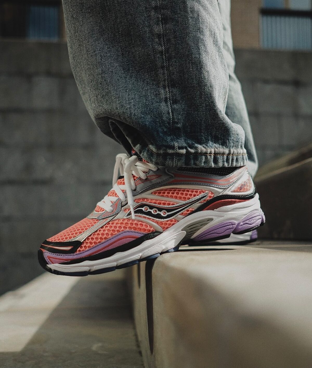 Close-up of pink, purple, and white Saucony ProGrid Omni 9 running shoes on a person's foot.