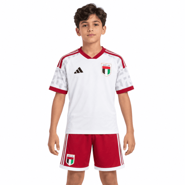 c8cbd45f-4cc0-4311-a8e9-bc7b858555c3 - UAE SPORT STORE Child wearing UAE national team kids' home football kit with white shirt and red shorts.