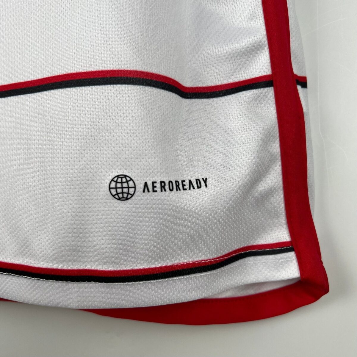 Close-up of white sports jersey with Aeroready logo and red trim.