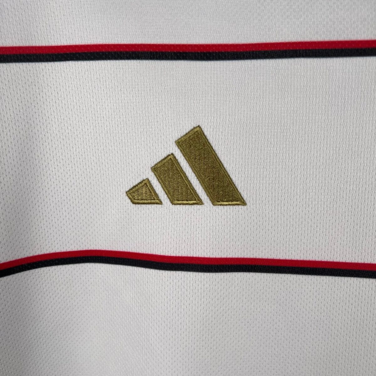 Close-up of a white sports jersey with gold Adidas logo and red and black stripes.