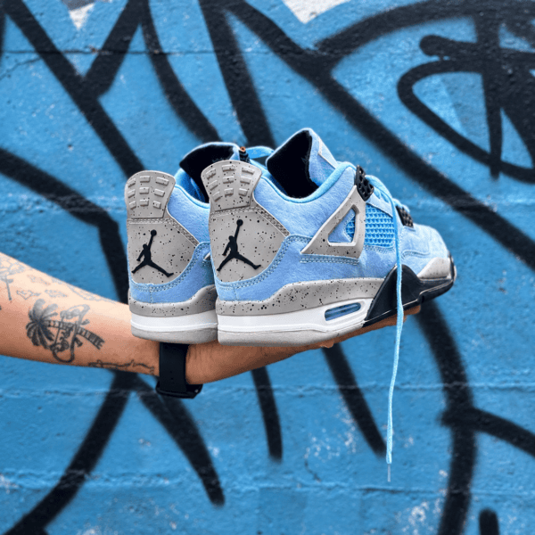 Blue and grey Air Jordan 4 Retro sneakers held against graffiti wall.