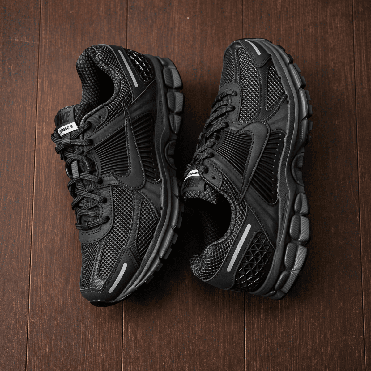 Nike Zoom Vomero 5 Triple Black running shoes on wooden floor.