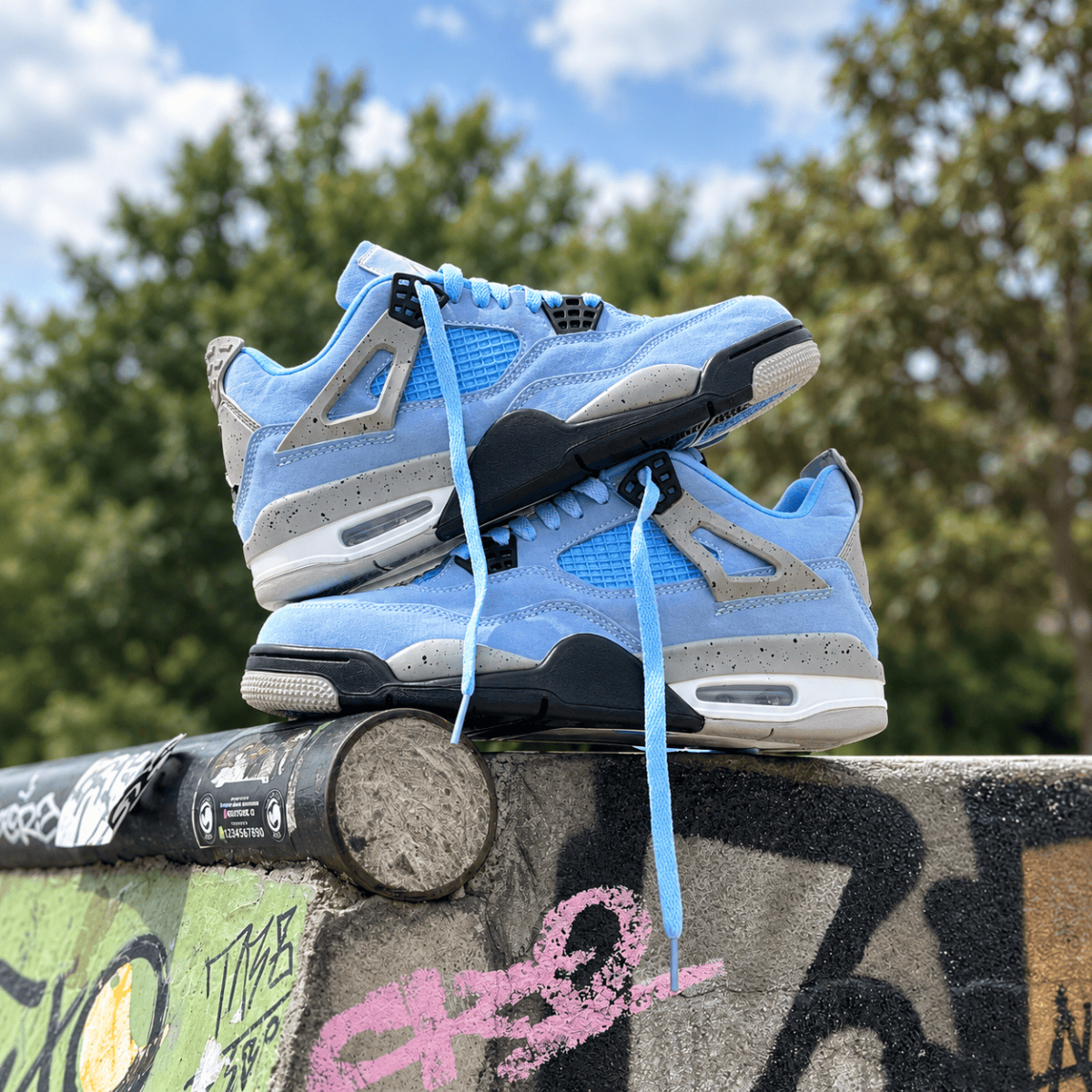 Light blue Air Jordan 4 Retro sneakers on graffiti-covered surface outdoors.