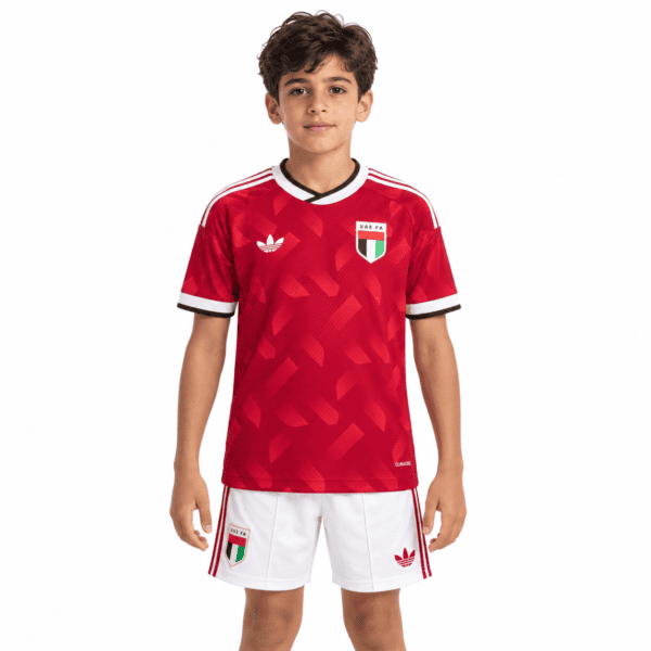 381569fd-8183-48e2-8069-b533255e8e8b - UAE SPORT STORE Young boy in UAE away kids 2026 football kit with red jersey and white shorts.