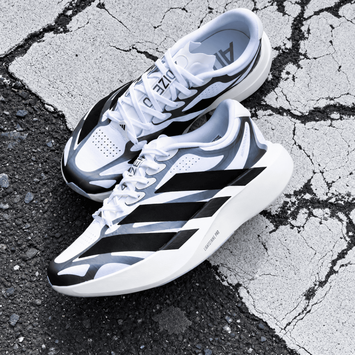 Adidas Adizero Evo SL EXO trainers in white and black on cracked pavement.