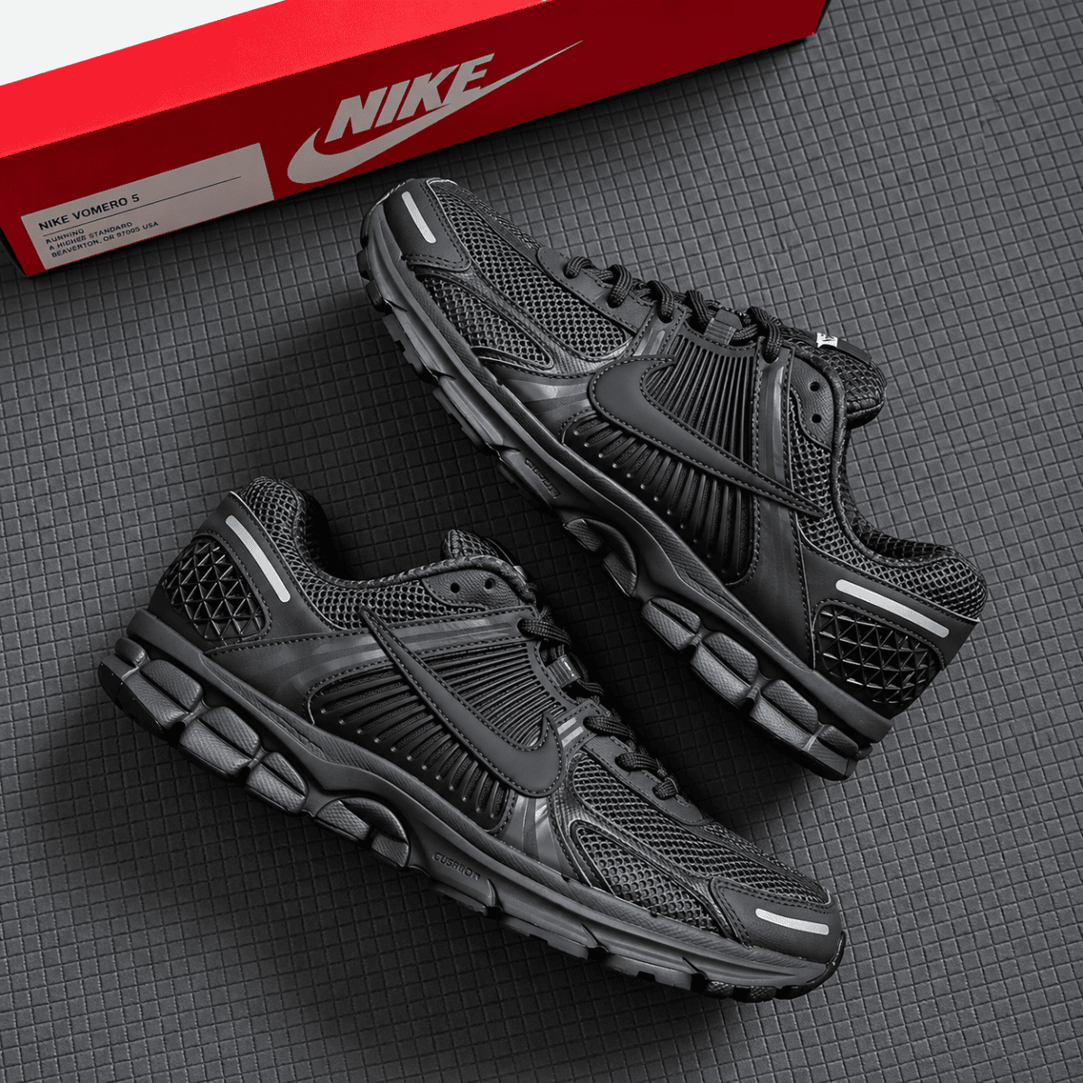 Nike Zoom Vomero 5 Triple Black running shoes on black surface with red box.