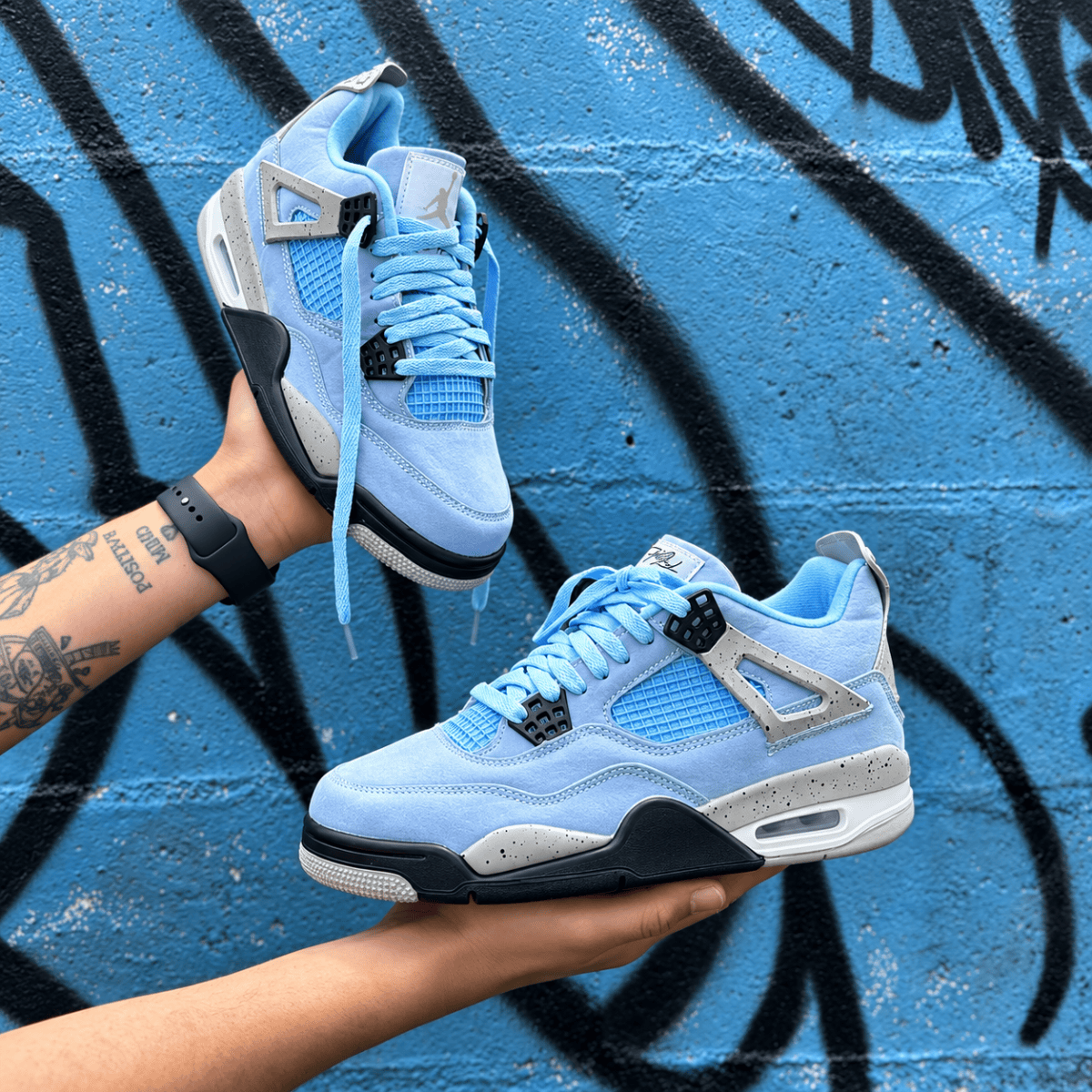 Light blue Air Jordan 4 Retro sneakers against graffiti wall background.