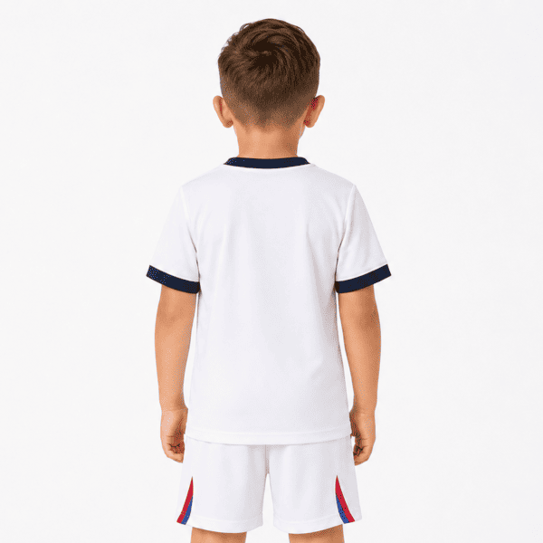 Child in white football kit with black trim, back view, plain white background.